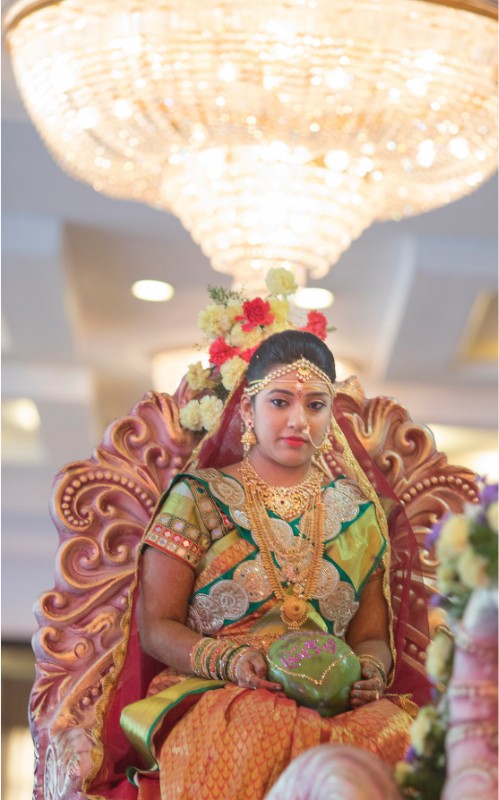 Bride in a green and gold silk saree seated on a carved throne beneath a crystal chandelier at a Hyderabad wedding
