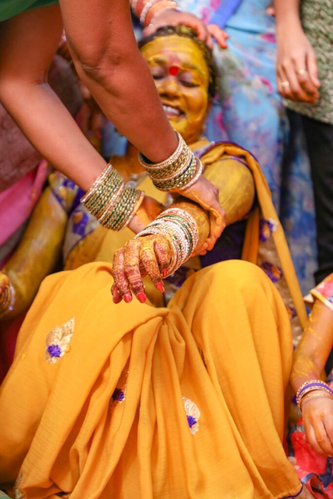 Bride smiling during a Telugu haldi ceremony as relatives apply turmeric – HydSharpFocus Hyderabad wedding photography