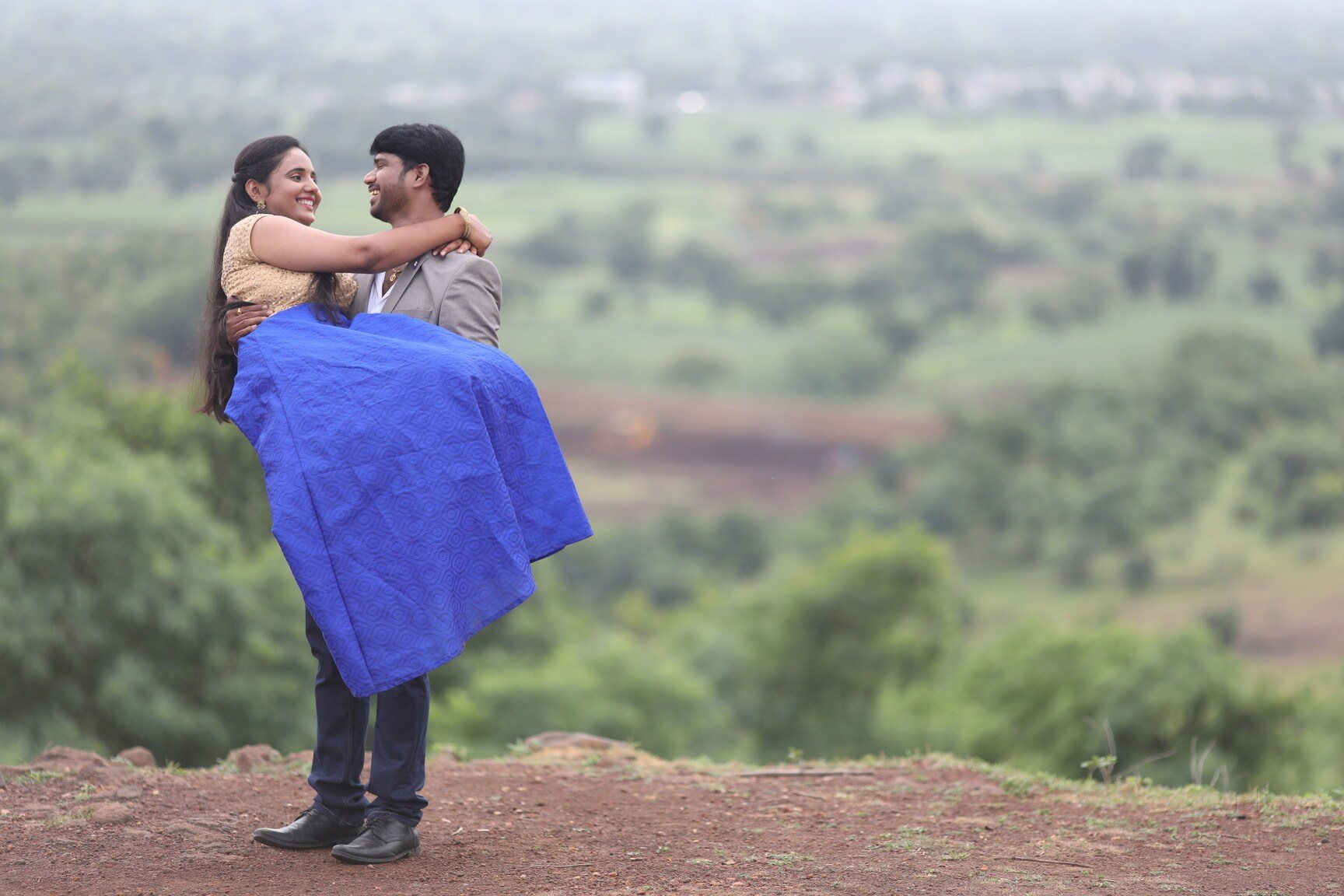Groom lifting his laughing bride-to-be on a hilltop overlooking green fields during a pre-wedding photoshoot in Hyderabad